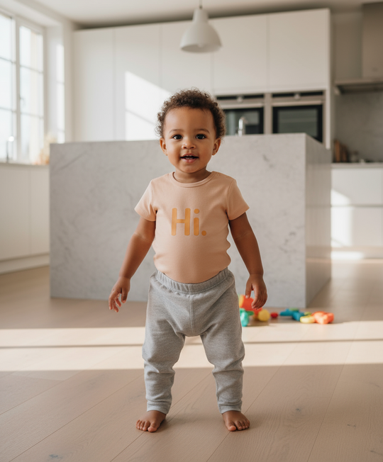 Child wearing a 'Hi' codysuit in a kitchen