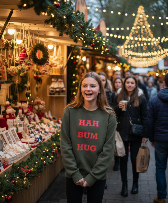 Woman in a festive market setting wearing a sweatshirt with text, surrounded by Christmas decorations and lights.