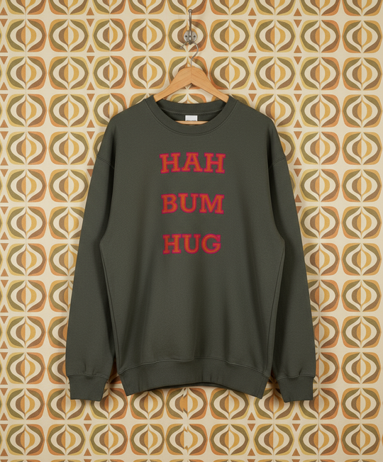 Green sweatshirt with red text 'HAH BUM HUG' on a hanger against a patterned wall.
