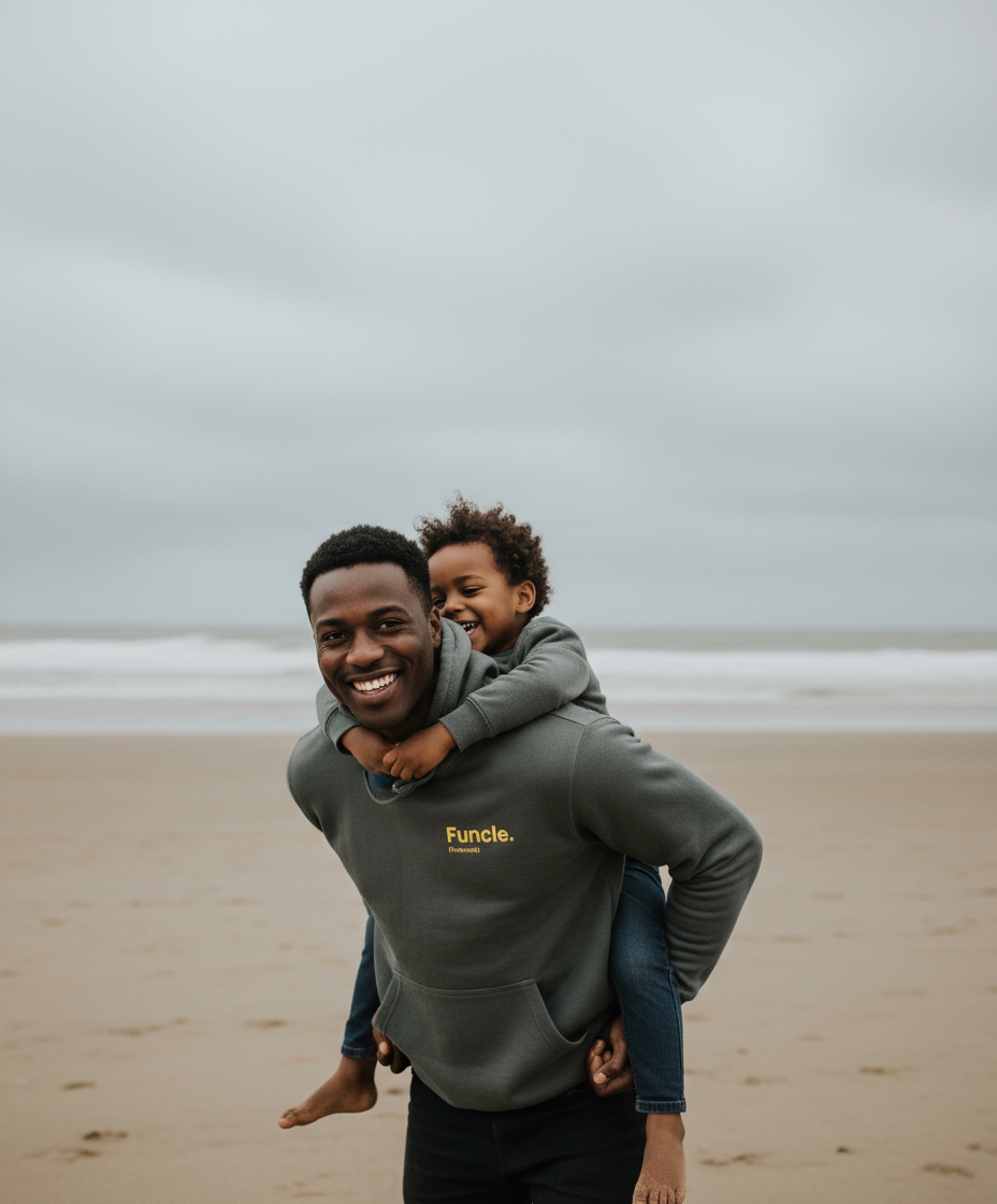 Man carrying a child on his shoulders at the beach, both wearing hoodies with visible branding.