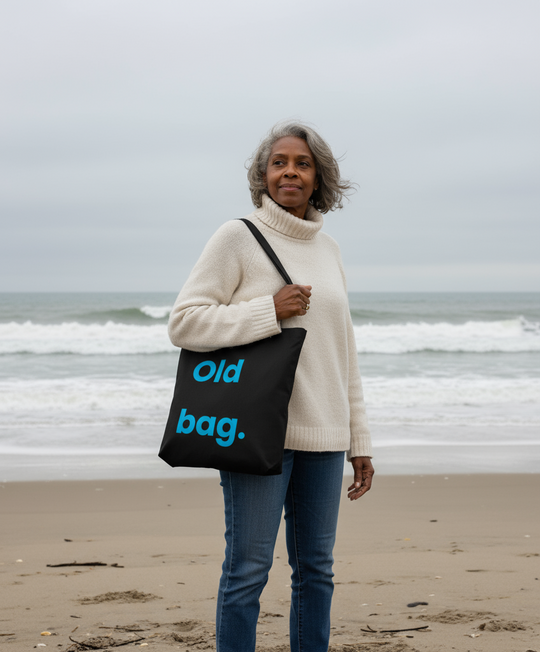 Woman on a beach holding a black tote bag with 'old bag.' text