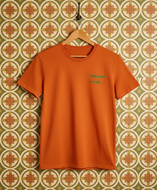 Orange t-shirt with text on a hanger against a patterned wall.