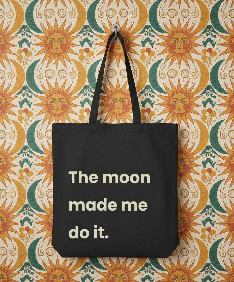 Black tote bag with 'The moon made me do it' text on a sun-patterned background