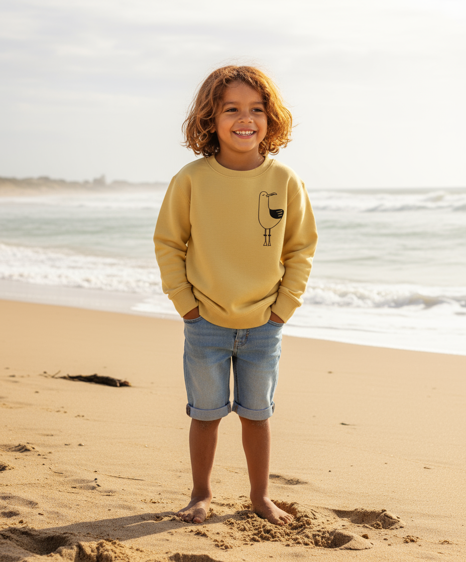 Child wearing a yellow sweatshirt with a design on a beach