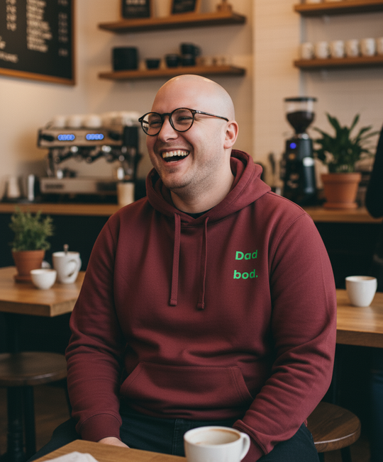 Man in a maroon hoodie with text sitting at a coffee shop counter, smiling.