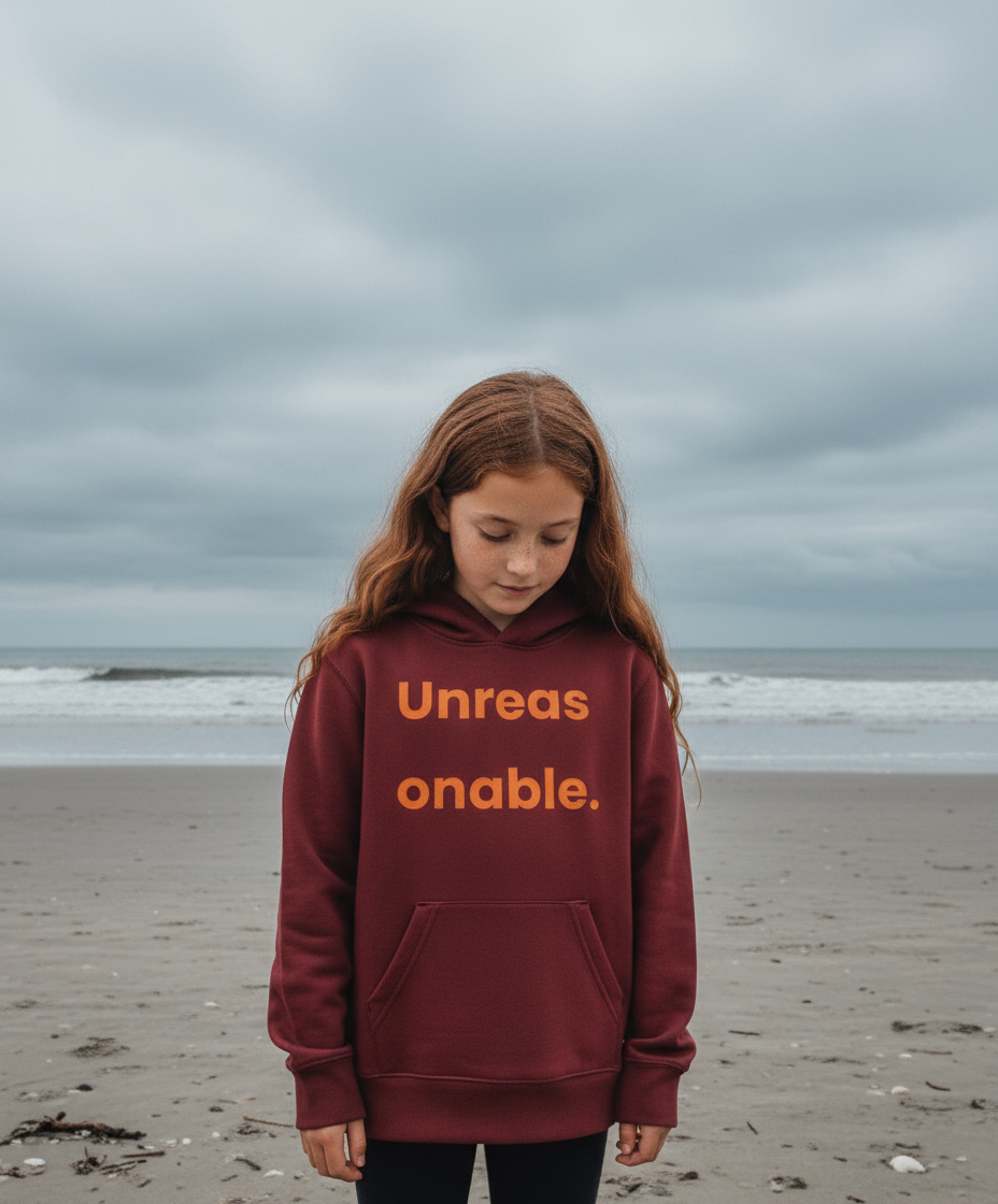Child wearing a maroon hoodie with 'Unreasonable' text on a beach