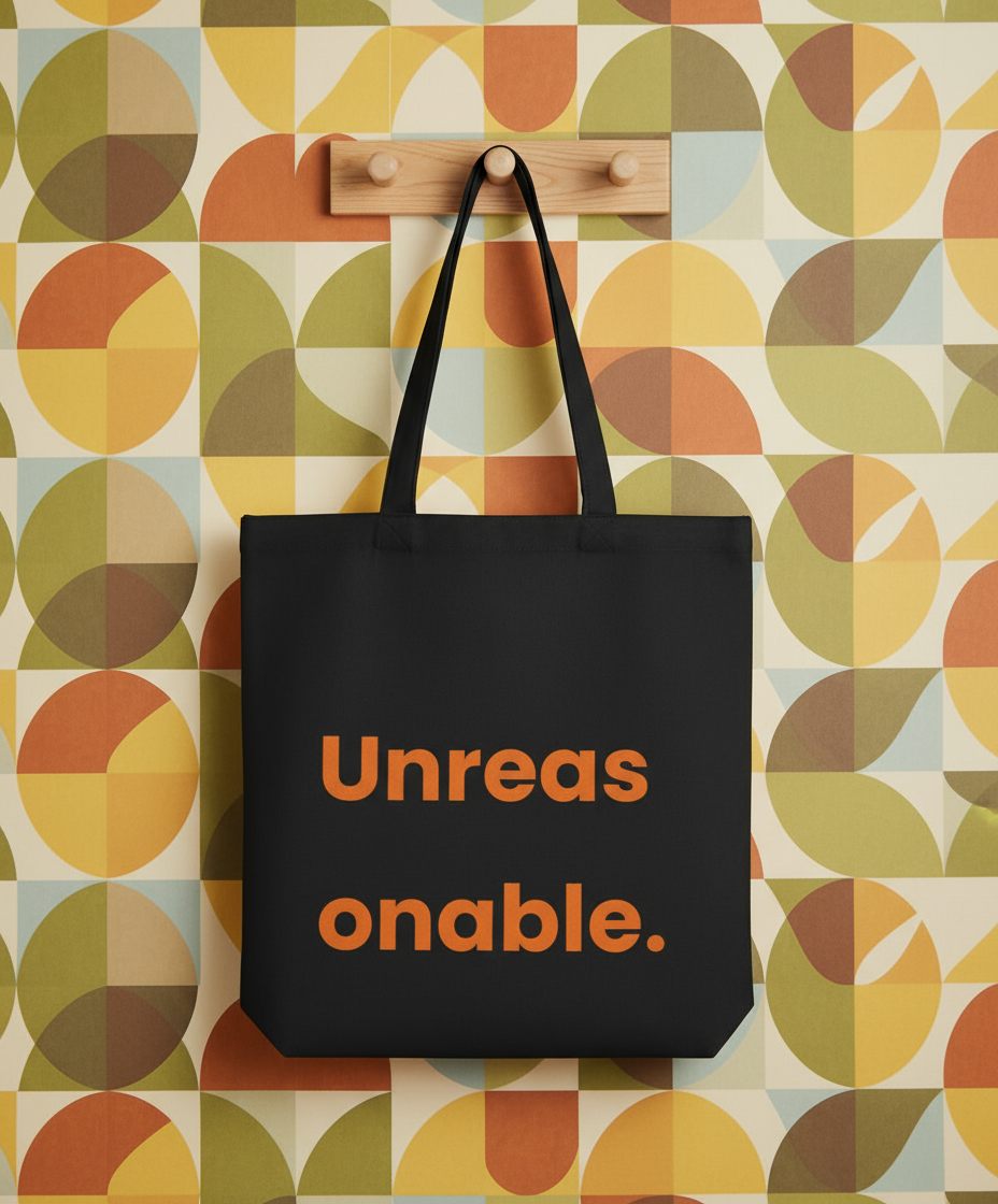 Black tote bag with 'Unreasonable' text on a colorful geometric-patterned wall.