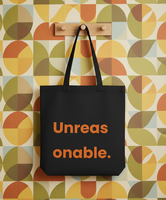 Black tote bag with 'Unreasonable' text on a colorful geometric-patterned wall.
