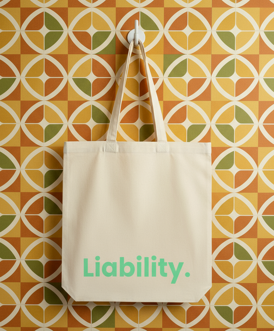 Beige tote bag with 'Liability.' text on a geometric patterned wall.