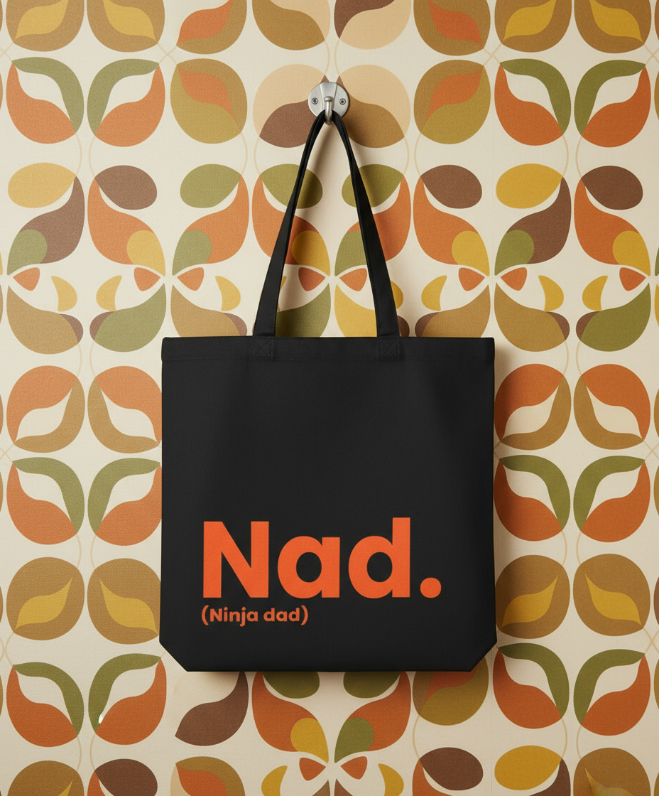 Black tote bag with 'Nad. (Ninja dad)' text on a patterned wall background
