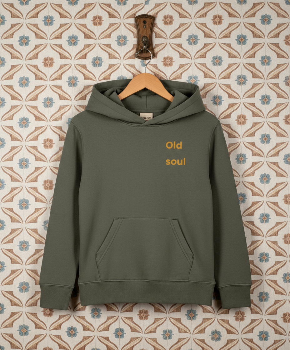 Green hoodie with 'Old soul' text on a hanger against a patterned wall.