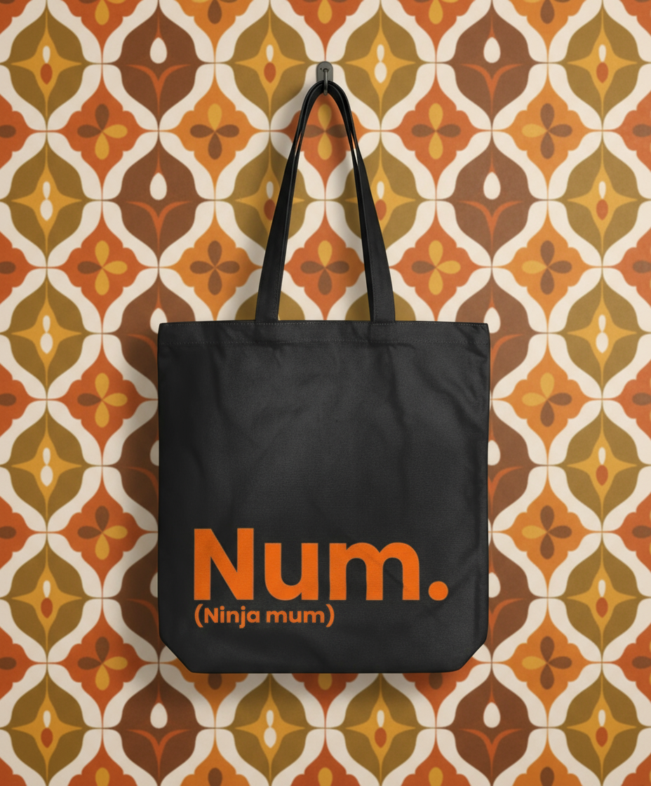 Black tote bag with 'Num. (Ninja mum)' text on a patterned wall background