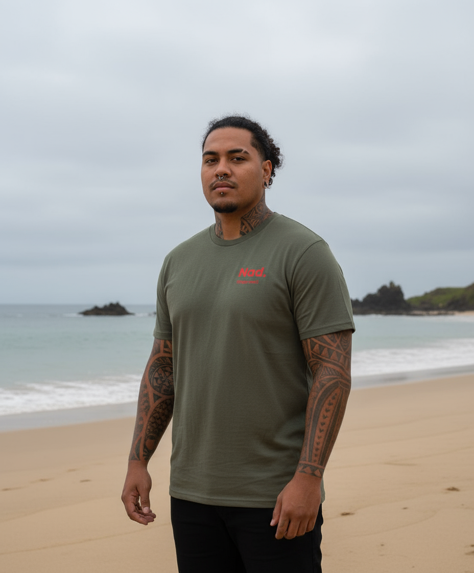 Man standing on a beach wearing a green t-shirt with red text