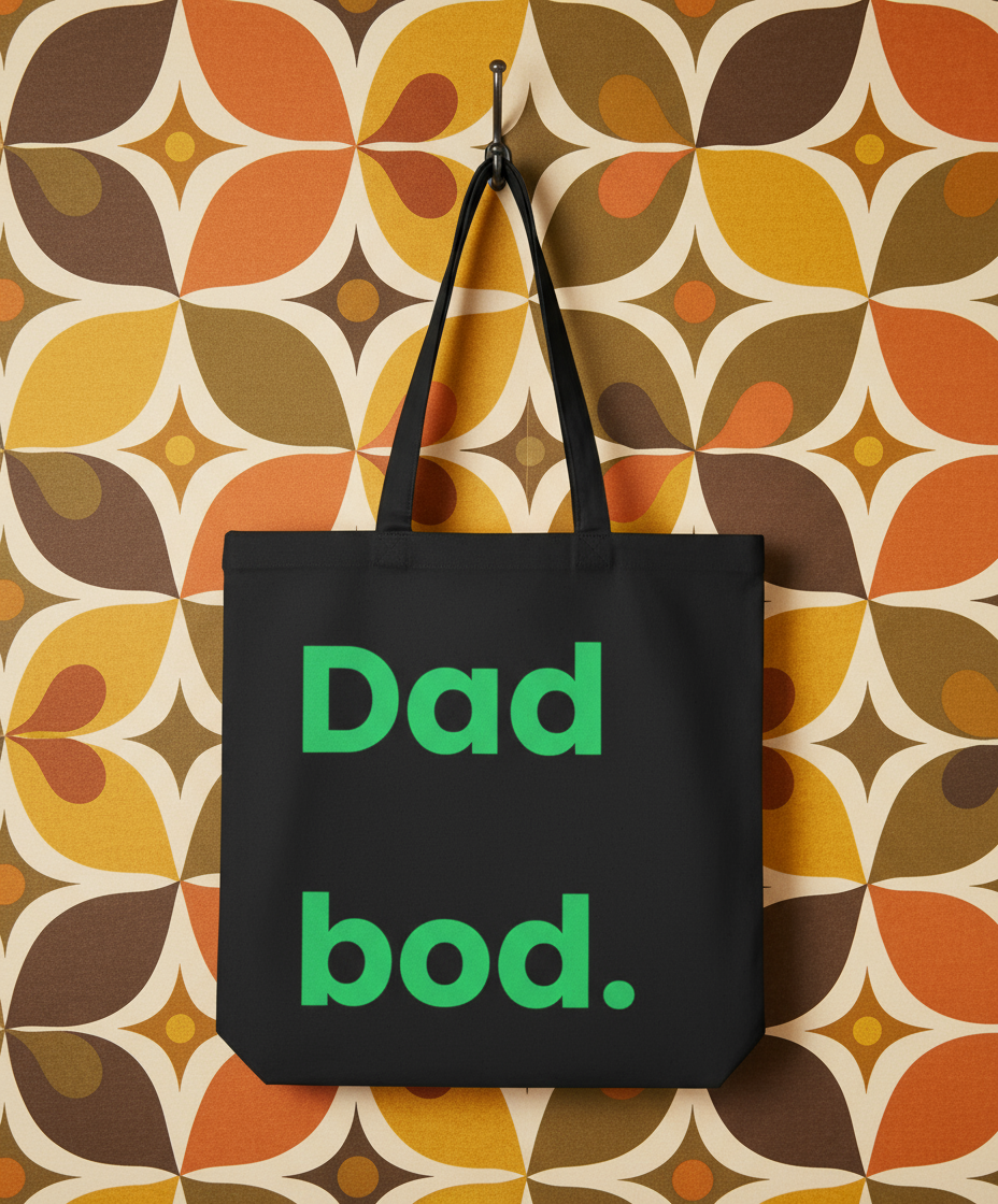 Black tote bag with 'Dad bod.' text on a patterned wall background
