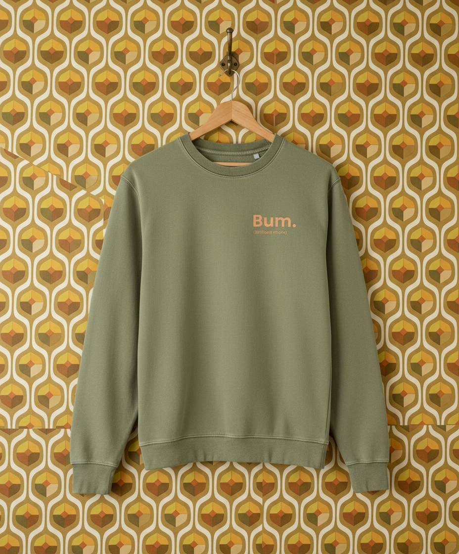 Green sweatshirt with 'Bum' text on a hanger against a patterned wall.