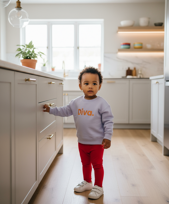 Child in a kitchen wearing a light purple sweatshirt with 'Diva' on it