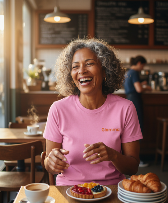 Woman in a pink 'Gamma' shirt laughing in a cafe with pastries on the table.