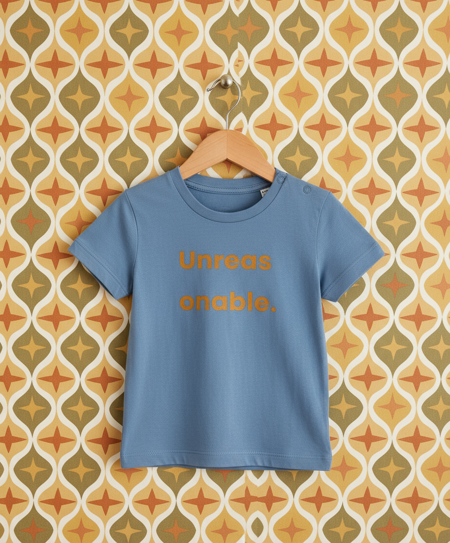 Blue t-shirt with 'Unreasonable' text on a hanger against a patterned wall.