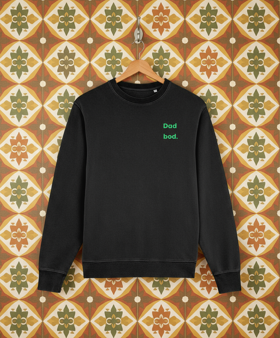 Black sweatshirt with 'Dad bod' text on a hanger against a patterned wall.