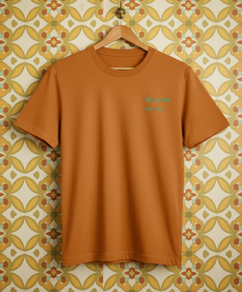 Orange t-shirt with green text on a hanger against a patterned wall