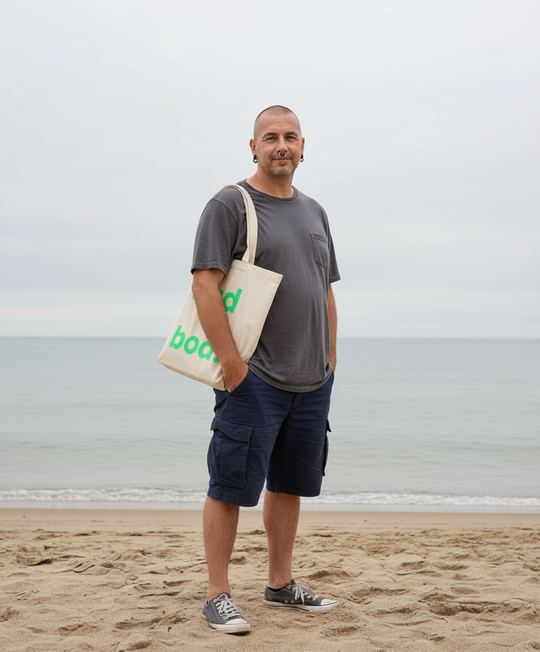 Man standing on a beach holding a tote bag with 'dad bod' printed on it.