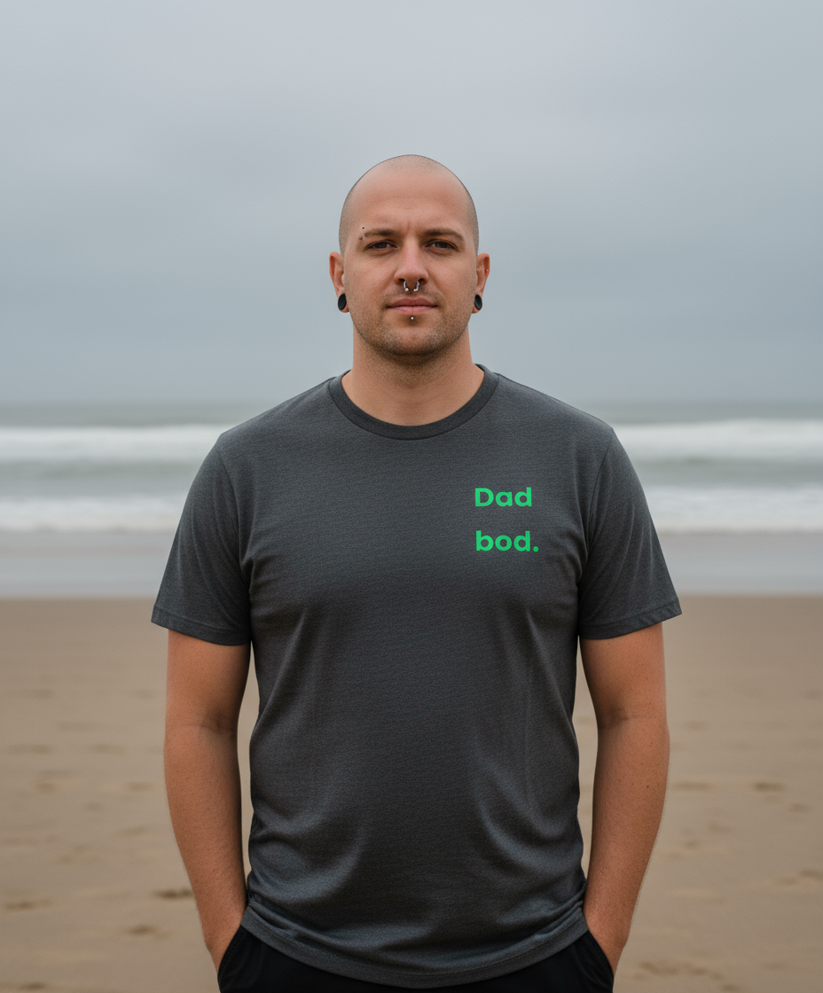 Man wearing a dark gray t-shirt with 'Dad bod.' text on a beach