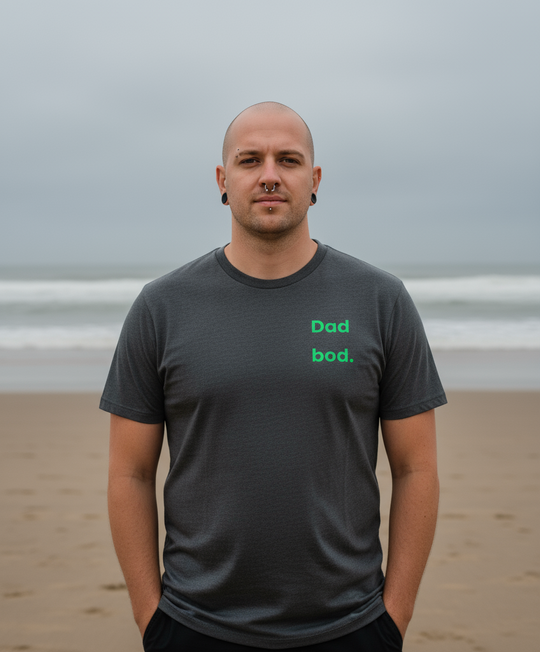 Man wearing a dark gray t-shirt with 'Dad bod.' text on a beach