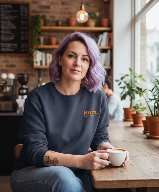 Person wearing a navy sweatshirt with 'Num.' logo, holding a coffee cup in a cozy cafe setting.