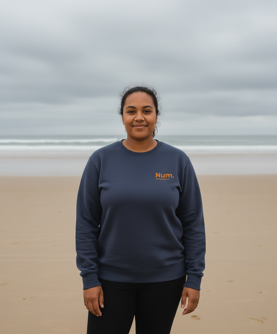Person wearing a navy sweatshirt with 'Num' logo on a beach