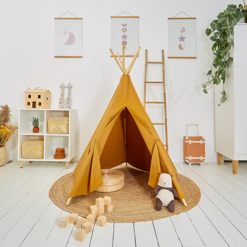 A yellow play teepee set up in a room with a wooden five-pole system, surrounded by children's toys and decorations on the walls.