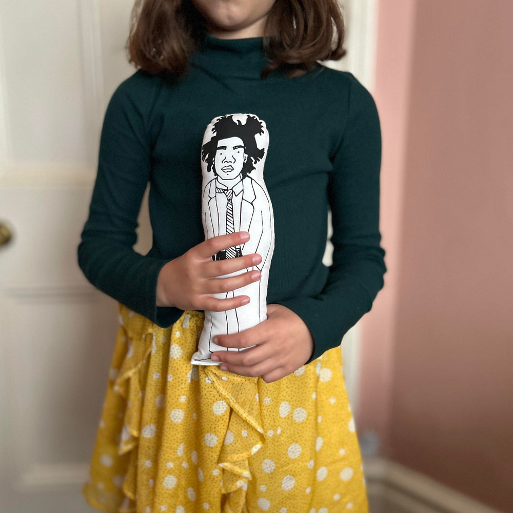 A child holding screen printed doll cushion of artist Jean Michel Basquiat