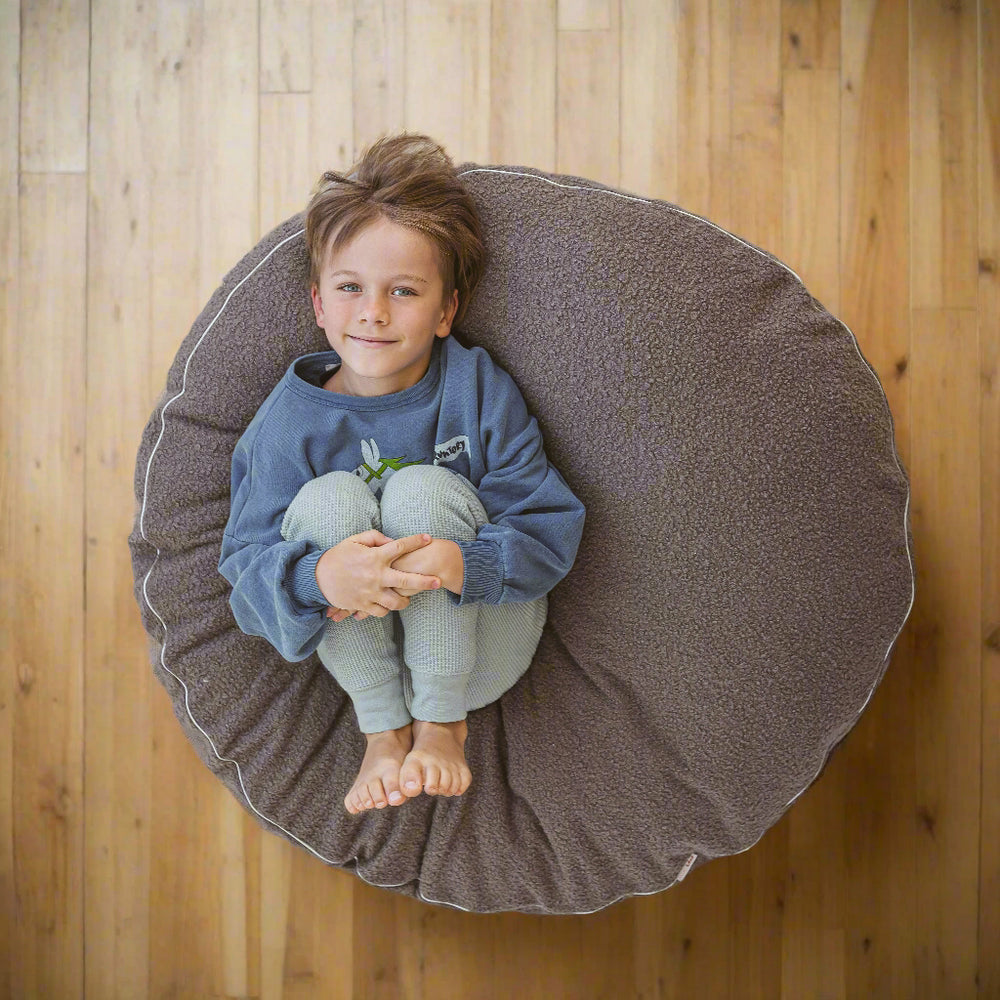 View from above of a child lying on grey floor cushion and holding his knees up to his chest