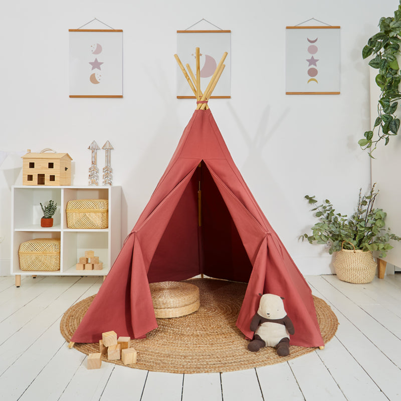 A rose-coloured play teepee made of cotton canvas, set up in a room with children's toys and decorations around it.