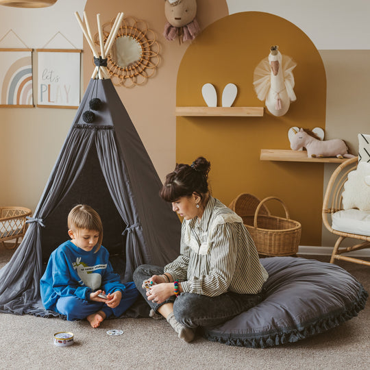 Woman and child playing together in a cosy room with a teepee and shelves.