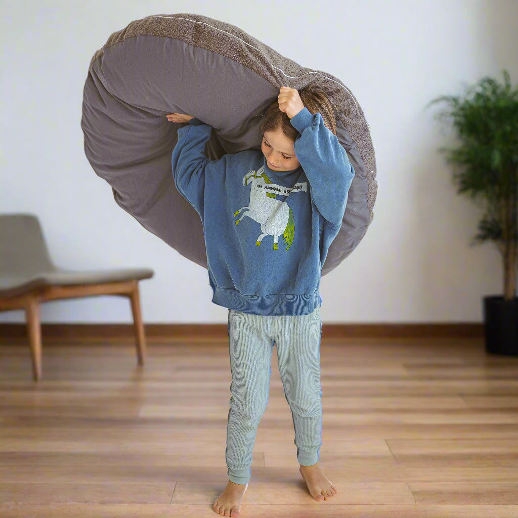 Child holding a large grey cushion above his head