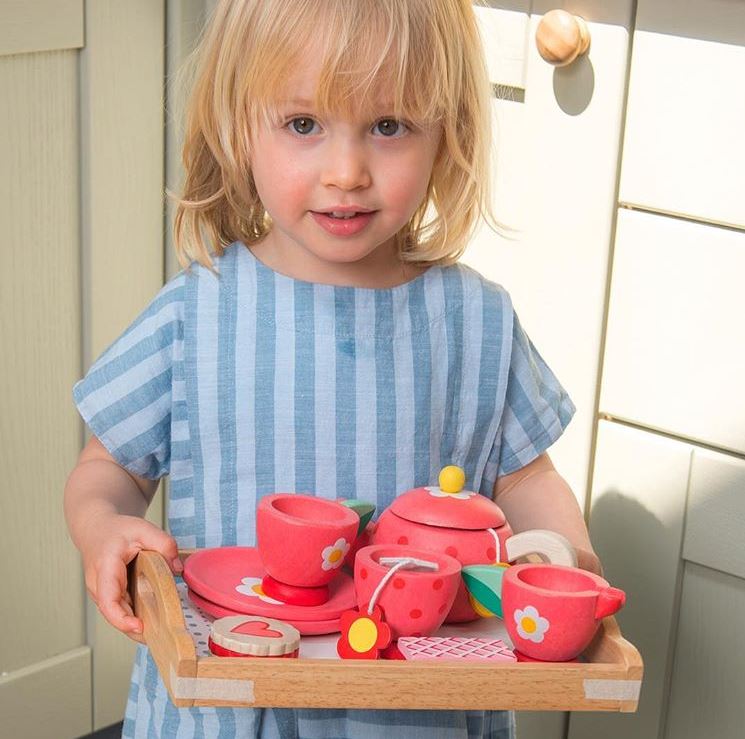 Child holding a toy tea set in a kitchen setting