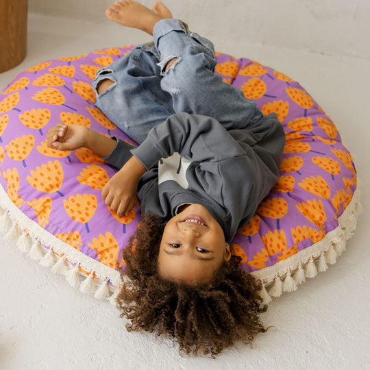 Child lying on a colourful round cushion with a purple and orange pattern