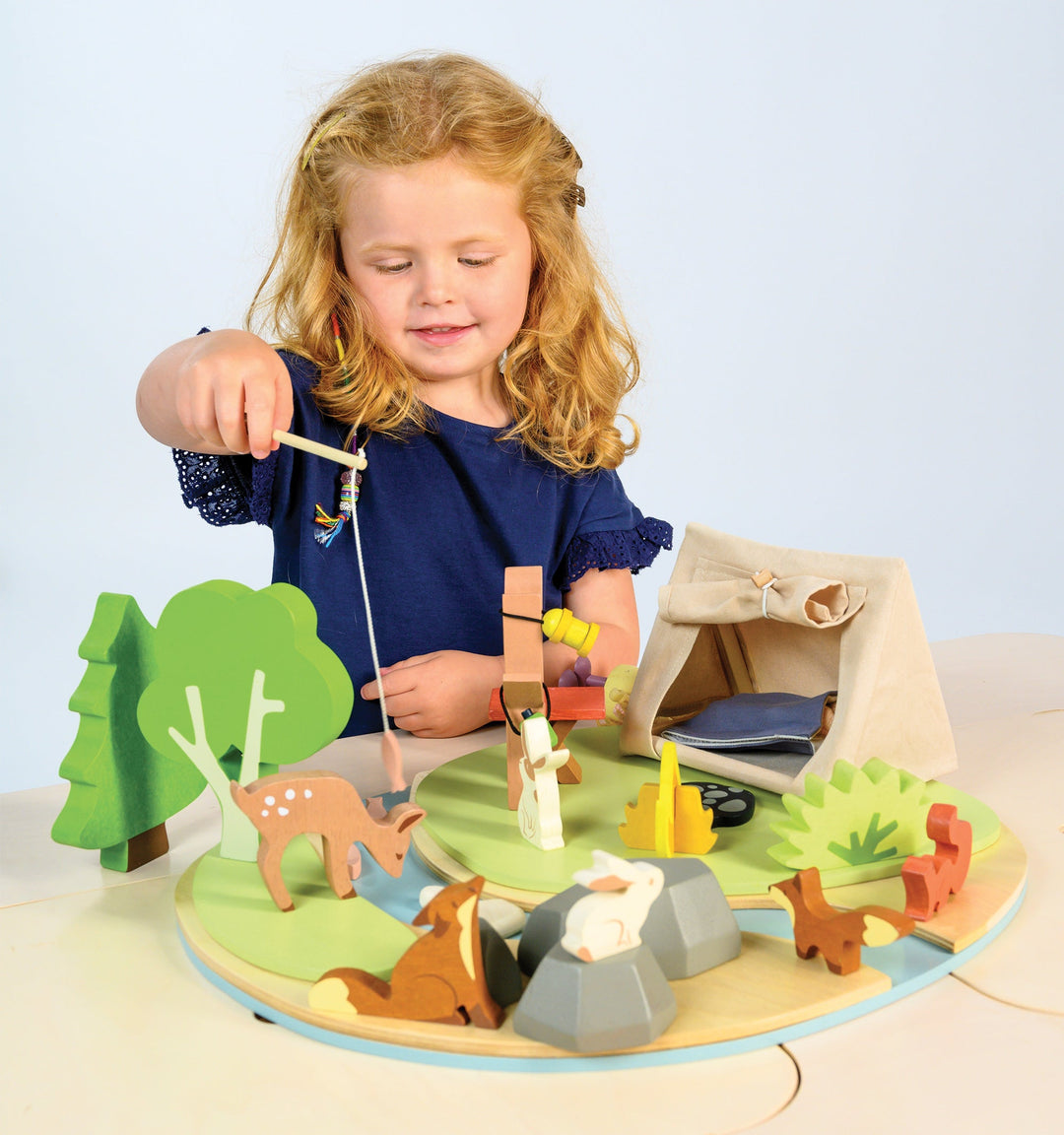 Child playing with a wooden camping scene toy set on a light blue background