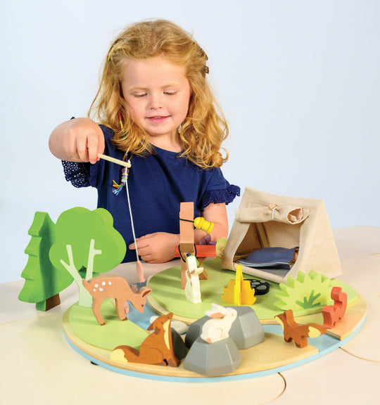 Child playing with a wooden camping scene toy set on a light blue background