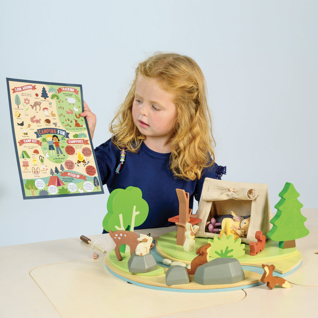 Child playing with a wooden playset featuring animals and trees, holding a map.